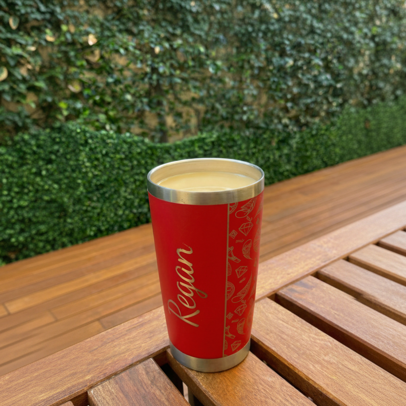 Red insulated tumbler with 'Regan' branding on a wooden table outdoors.